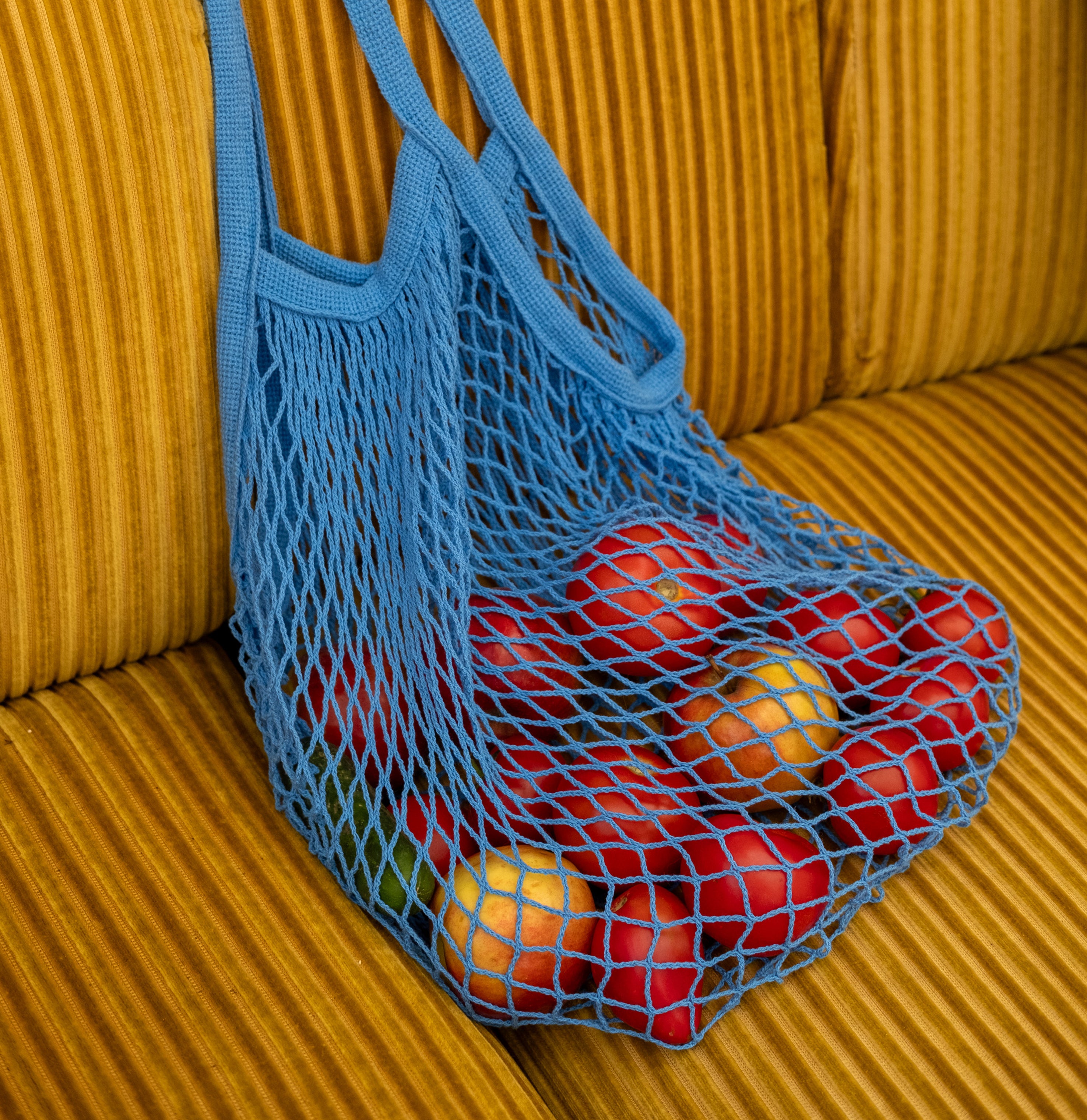 Rezginė sietka pirkinių krepšys mėlynos spalvos, su vaisiais viduje, ant sofos, dovanų idėjos, mados aksesuarai moterims