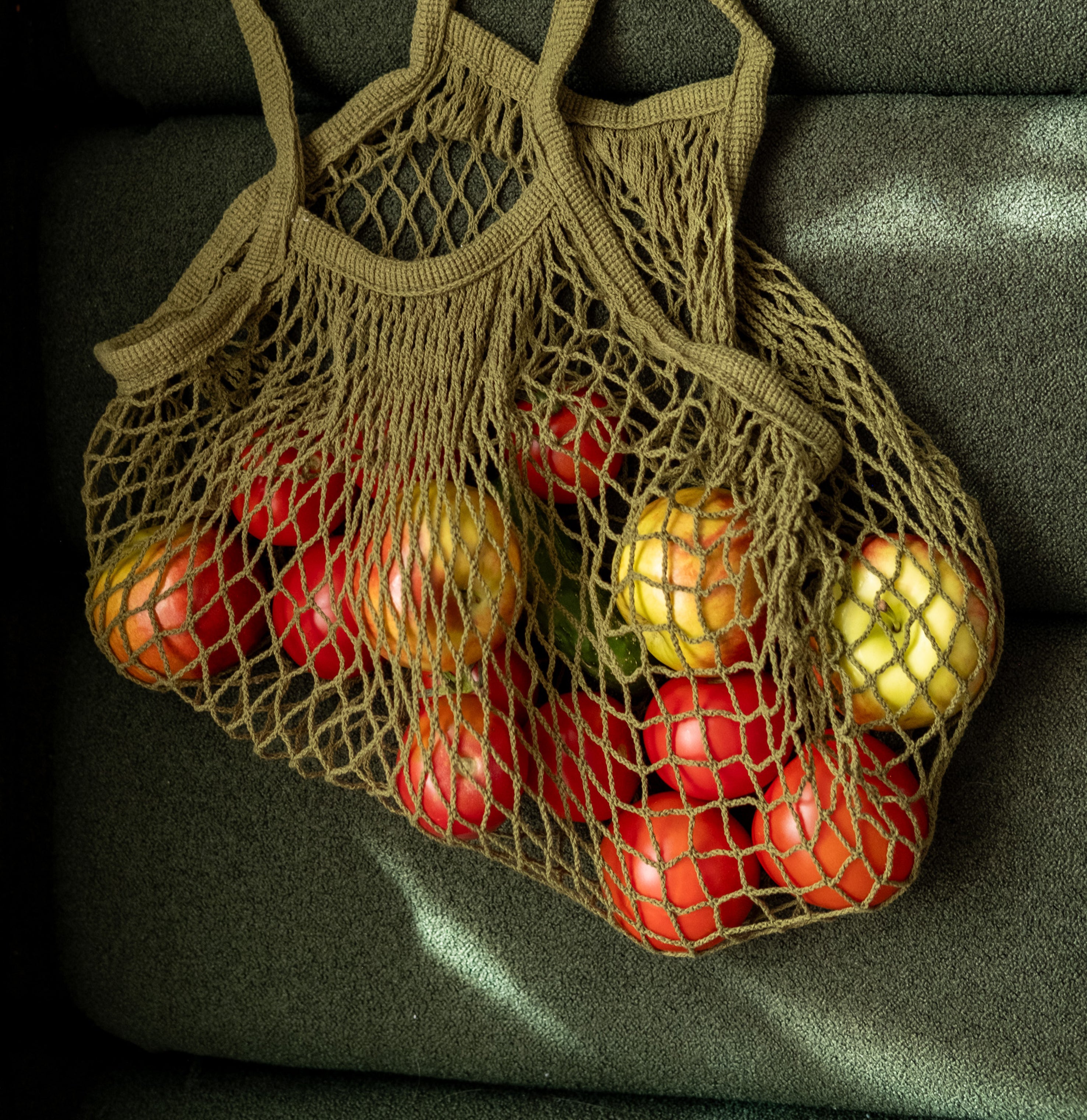 Rezginė sietka pirkinių krepšys samanų spalvos, su vaisiais viduje, ant sofos, dovanų idėjos, mados aksesuarai moterims